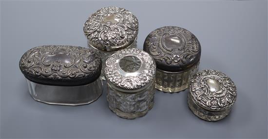 Five assorted early 20th century repousse silver mounted toilet jars, largest 8cm.